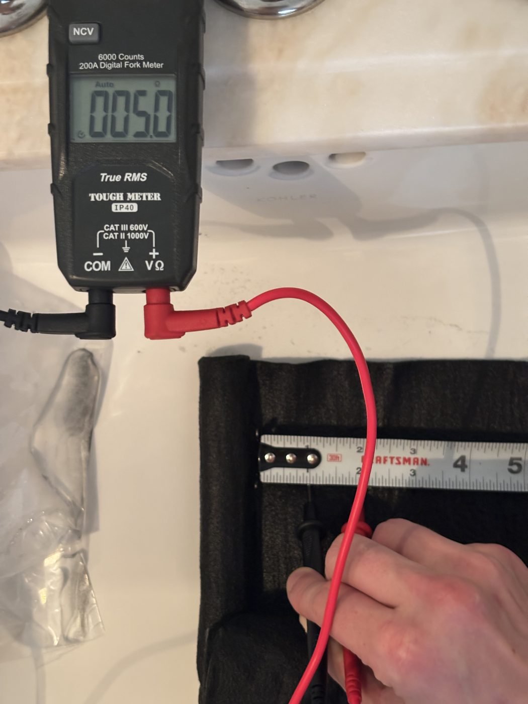 Multimeter reading 5.0 ohms with probes on the carbonized felt beside a tape measure