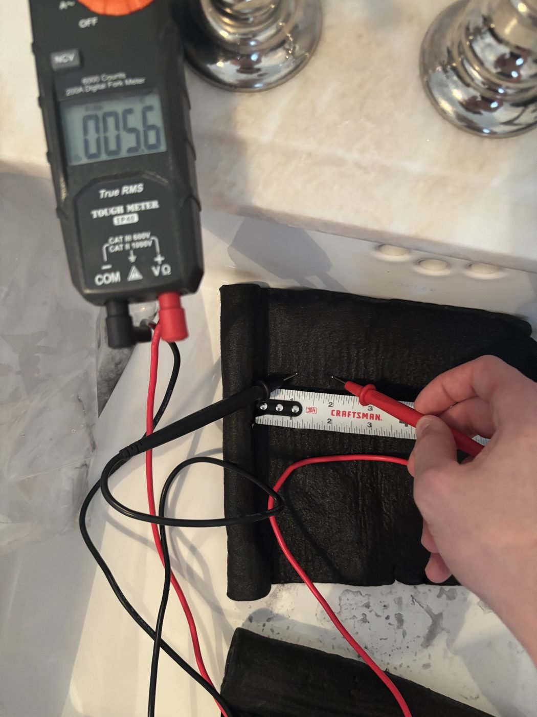 Multimeter reading 5.6 ohms with probes on a second spot of the carbonized felt beside a tape measure