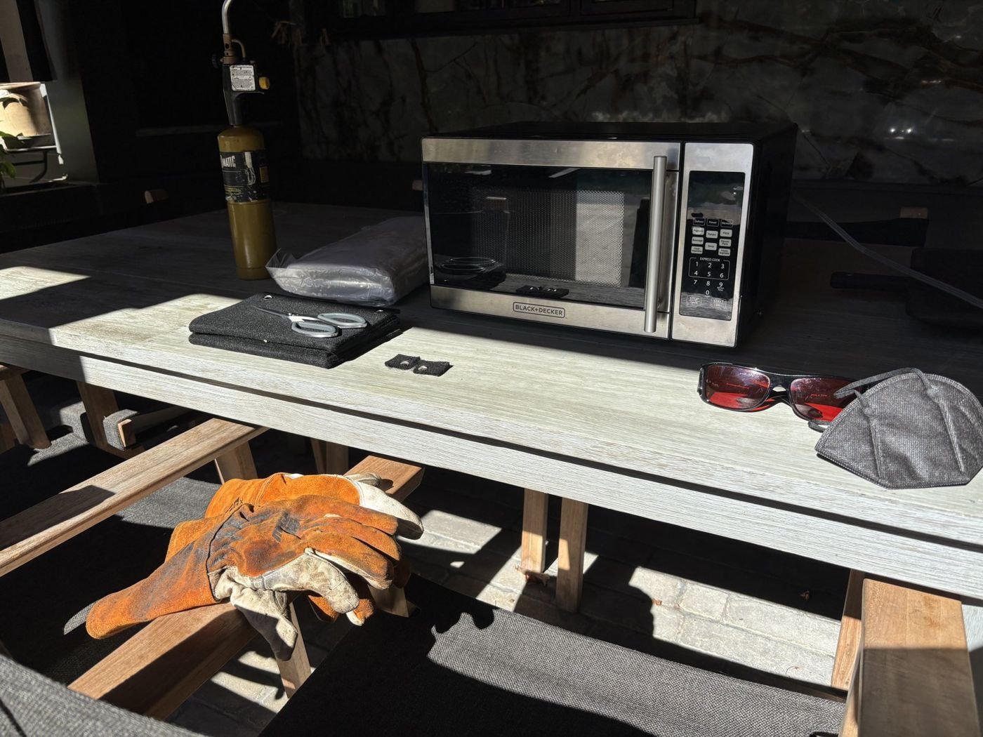 Outdoor work table with a microwave, welding-style gloves, a mask and tinted glasses laid out